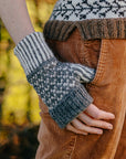 A close up image of a hand knitted wristwarmer made using grey and white undyed British Wool. The mitt has a 2 colour ribbing at the wrist and thumb, a 2 colour stranded colourwork design on the hand and a folded brim at the fingers.