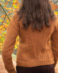 A 'from behind' shot of a person outdoors in an autumnal forest setting wearing a rust-coloured, textured handknit sweater.
