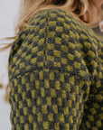 A close up shot of the drop shoulder of a green checkered handknit sweater made using hand dyed british wool yarn.