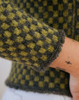 A close up shot of the tassel cuff detailing on a green checkered handknit sweater made using hand dyed british wool yarn.