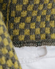 A close up shot of the tassel cuff detail on a green checkered handknit sweater made using hand dyed british wool yarn.