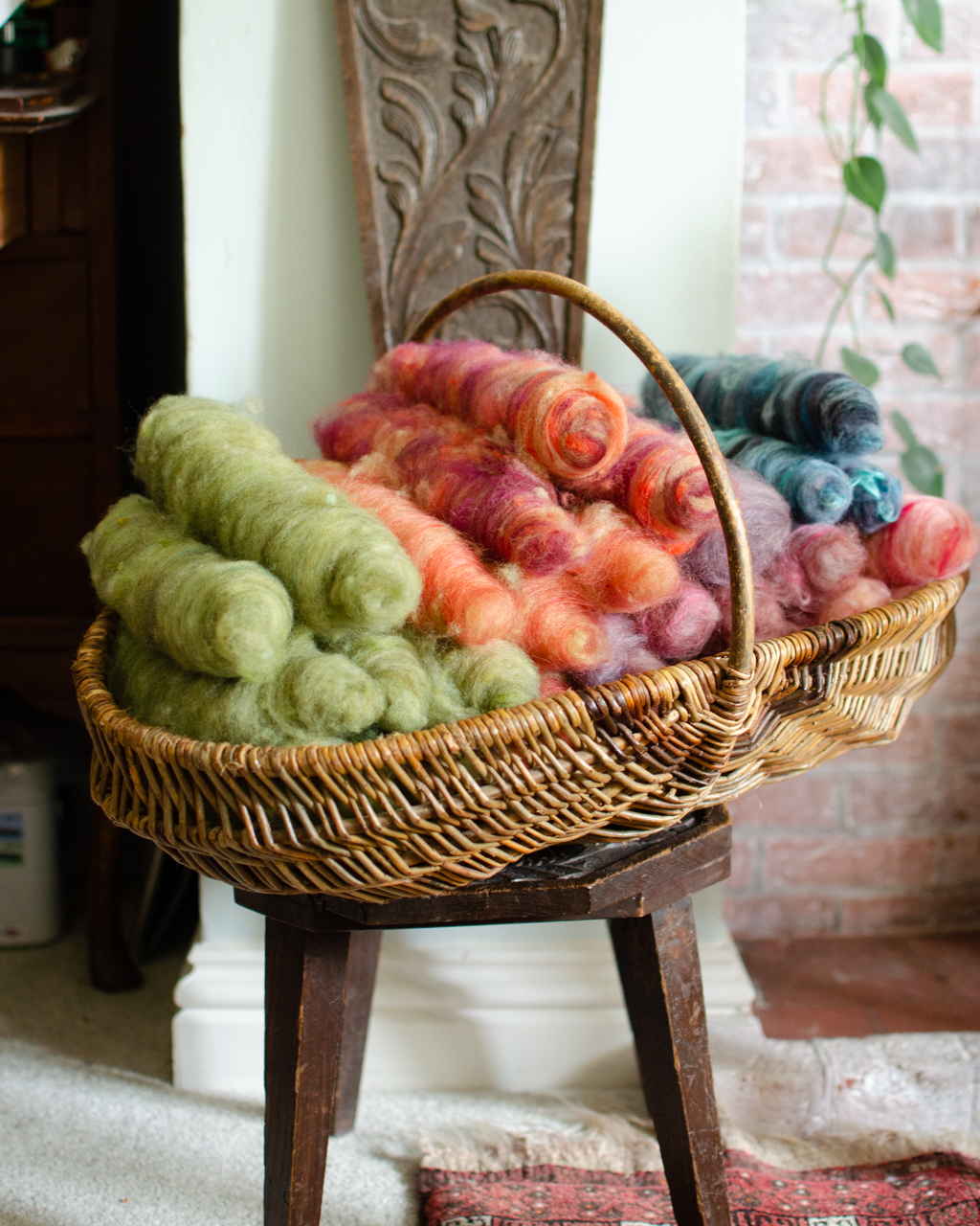 A basket of colourful fibre batts in a basket on a carved wooden chair. 