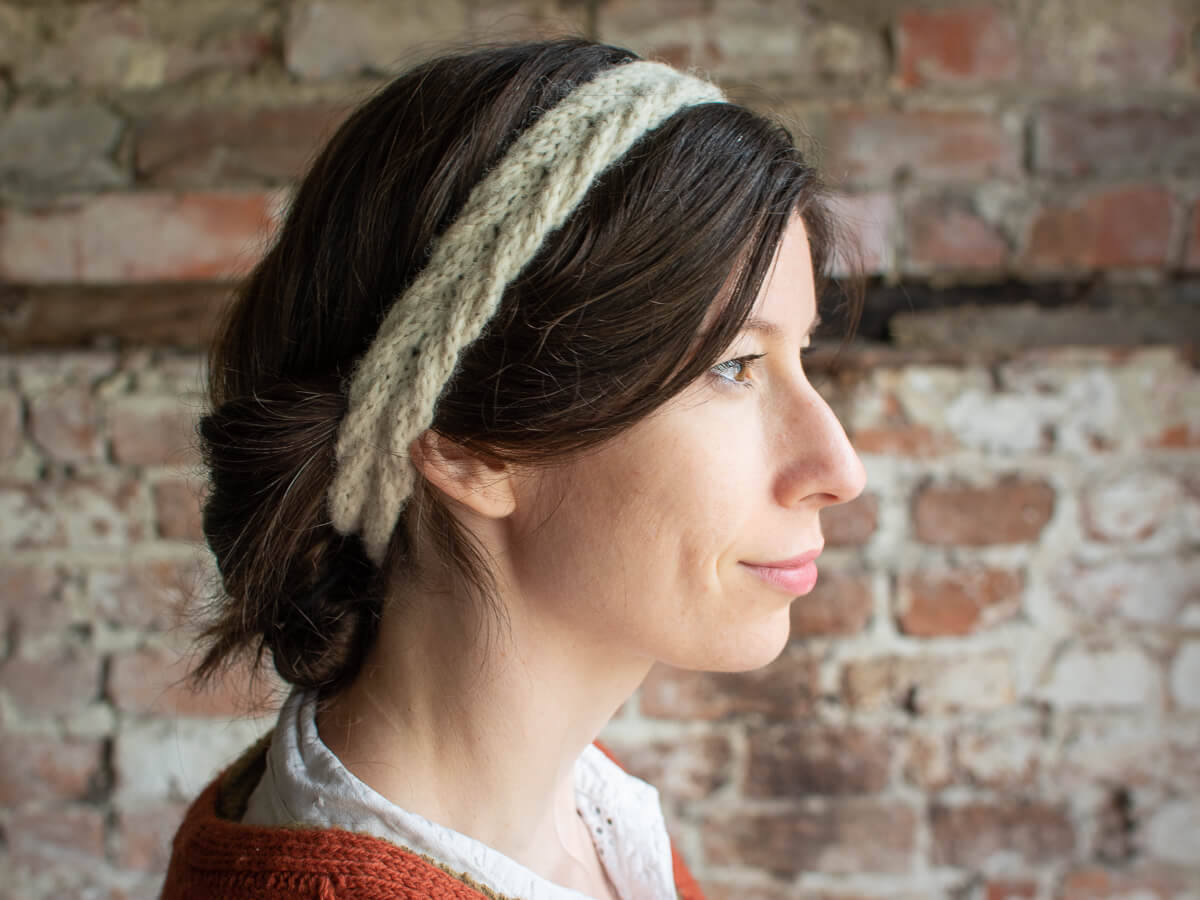 A close up shot of Marina wearing the Bournlet headband. She is side on to the camera, her hair is tied back to showcase the cream, cable knit headband