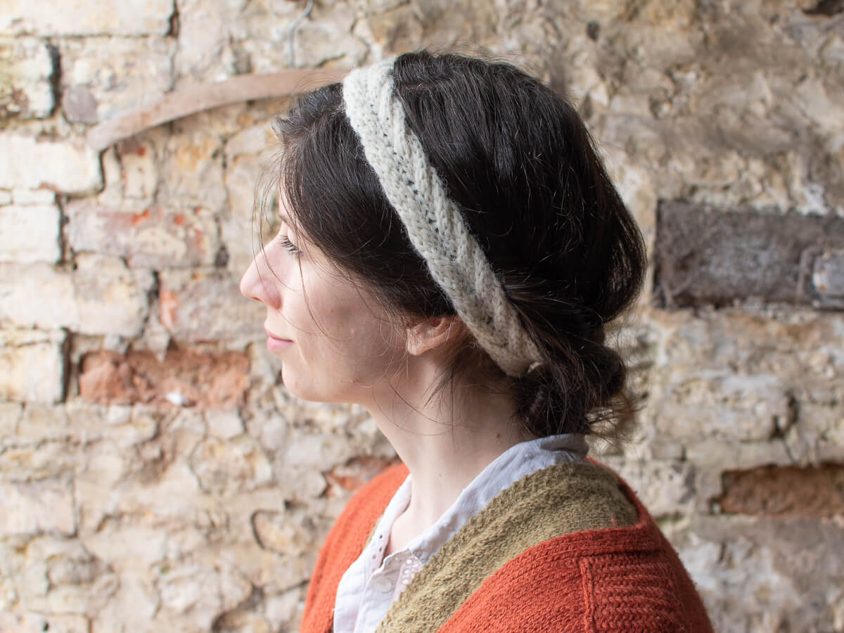 A close up shot of Marina wearing the Bournlet headband. She is side on to the camera, her hair is tied back to showcase the cream, cable knit headband