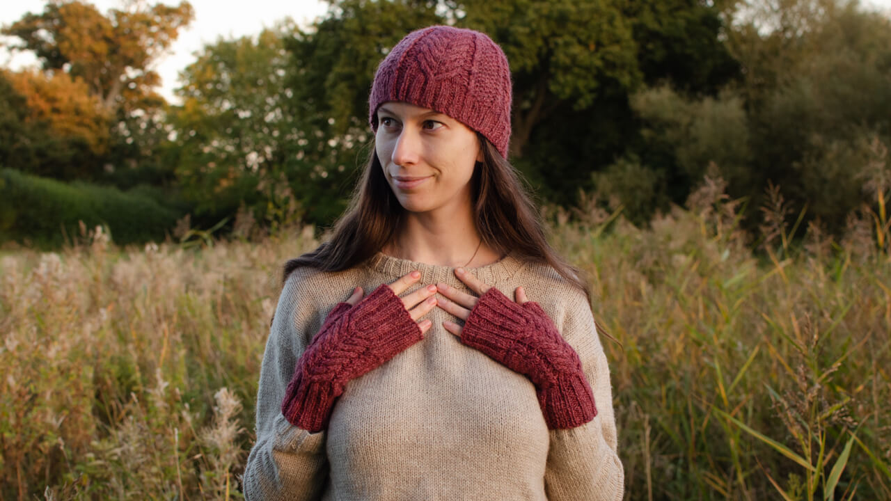 A matching set of cabled hat and fingerless mitts in dark pink hand-dyed yarn, with a hand-knitted jumper in beige undyed British wool