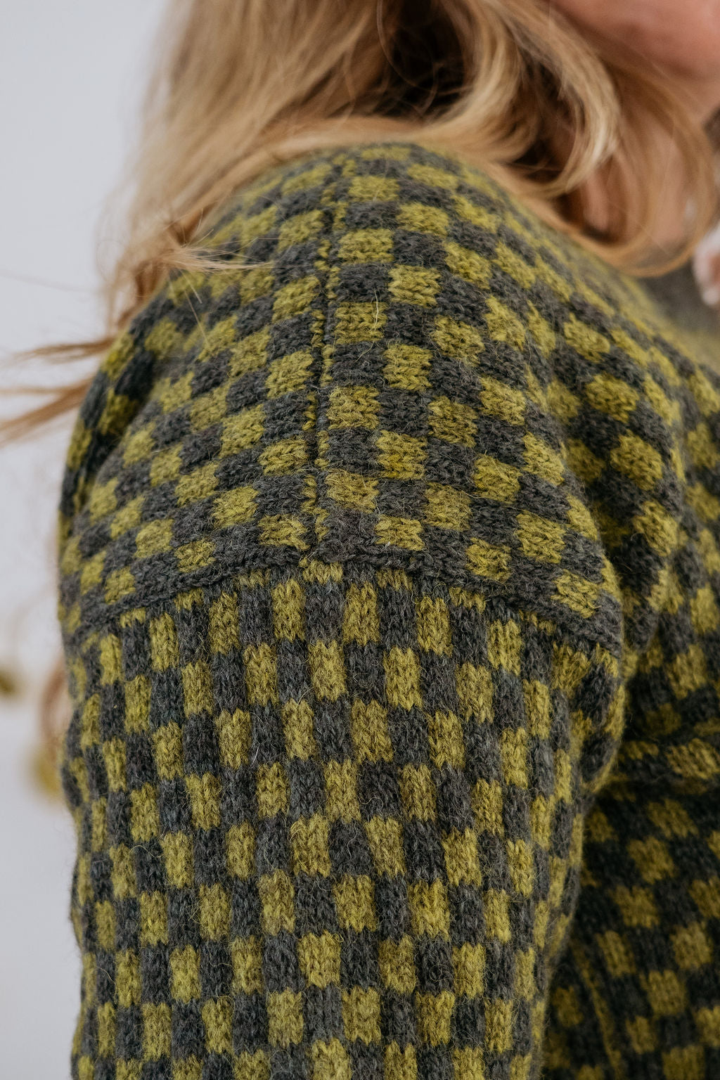 A close up shot of the drop shoulder of a green checkered handknit sweater made using hand dyed british wool yarn.