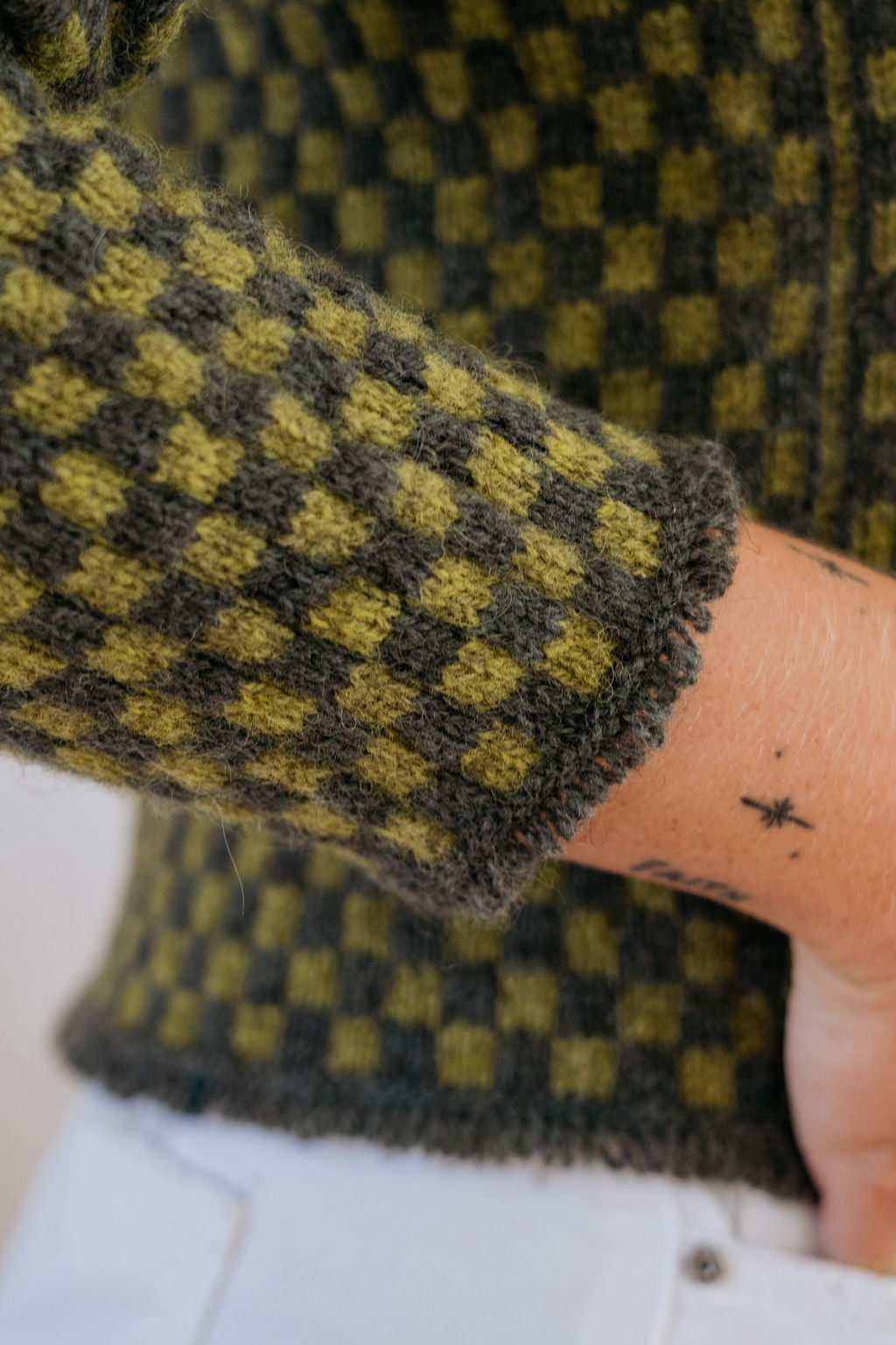 A close up shot of the tassel cuff detailing on a green checkered handknit sweater made using hand dyed british wool yarn.