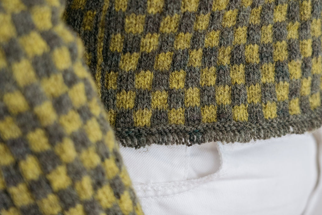 A close up shot of the tassel cuff detail on a green checkered handknit sweater made using hand dyed british wool yarn.