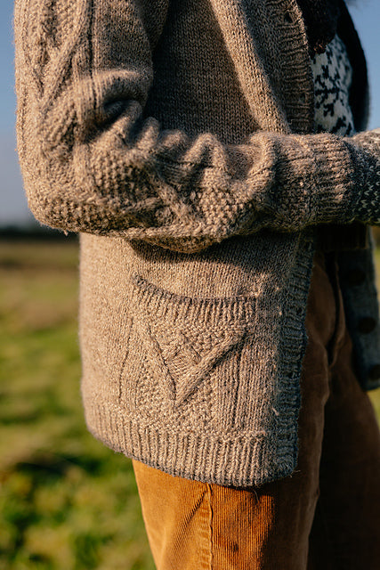 A close up shot of the cosy handknit grey cardigan marina is wearing. The focus is on the textured knit and cables on the pockets and sleeves