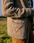 A close up shot of the cosy handknit grey cardigan marina is wearing. The focus is on the textured knit and cables on the pockets and sleeves
