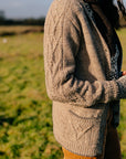 A torso shot of marina standing in a field outside. She is wearing a textured handknit grey cardigan and a dark brown scarf